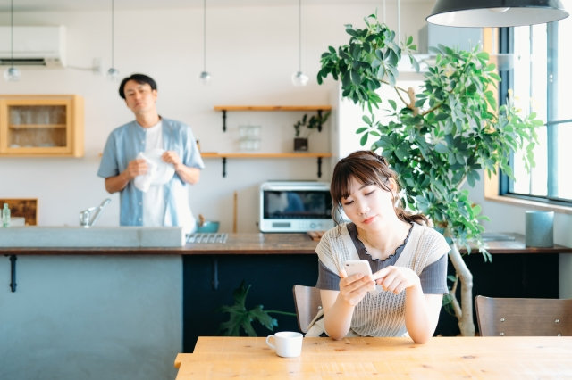 家事をしている夫とスマホを見ている妻